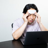 在宅勤務中に頭痛がひどくてこめかみを抑える男性の写真