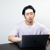発熱しながらも在宅ワークを続ける男性のデスクワークの写真