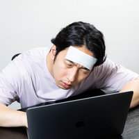 肘をつきながら在宅ワークする発熱中の男性の写真
