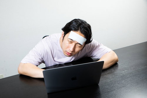 おでこを冷やして寝落ちしそうな在宅ワーカーの男性