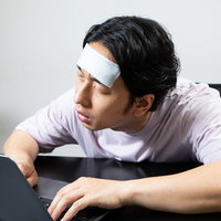 具合が悪くてデスクで居眠りする男子社員の疲労の写真