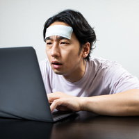 残業後、自宅に帰ってからも仕事をする体調不良の男性の写真