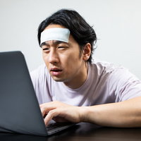 おでこを冷やして最後の力を振り絞る在宅ワーカー男性の写真