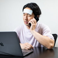 副反応で仕事を休むと連絡をする在宅勤務の男性の写真