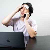 額に冷却シートを貼って遠くを見つめる在宅ワーカーの写真