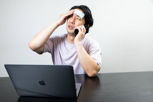 額に冷却シートを貼って遠くを見つめる在宅ワーカー