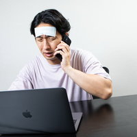 冷えピタを貼って仕事する過労の男性のデスクワークの写真