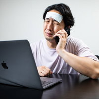 体調不良で発熱しながらクライアントの改修案件に泣きっ面で対応する男性エンジニアの写真
