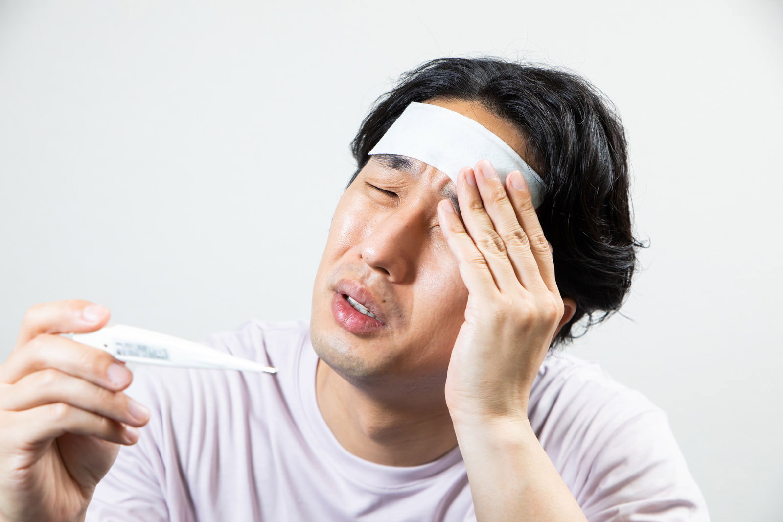 額に冷却シートを貼り体温計を持つ男性