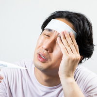 風邪をひいておでこを冷やしながら頭痛に苦しむ男性の写真