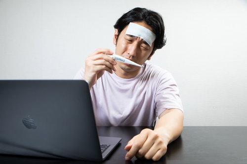 額に冷えピタを貼った体温計を見つめて仕事が手につかない男性