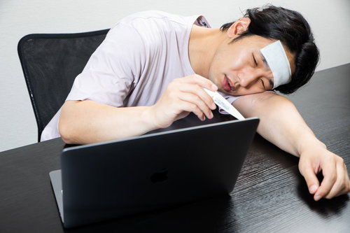高熱でうなだれるデスクワーク中の在宅ワーカー