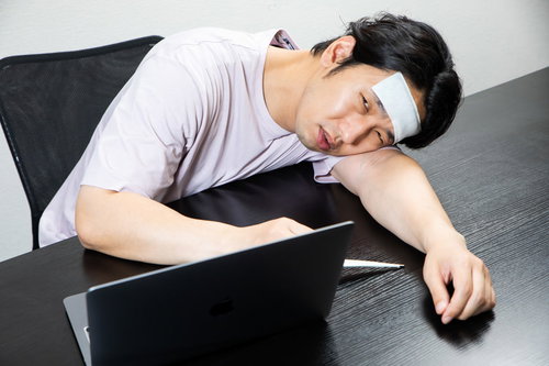 仕事中に机でぐったりして体温計を持つ高熱男子