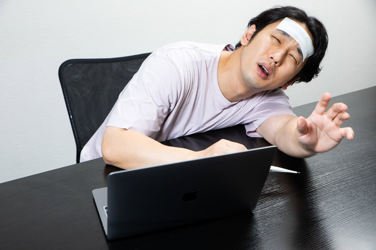 デスクで体温計を持ち冷えピタを貼って高熱でぐったりしている男性［モデル：大川竜弥］