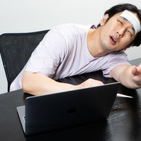 デスクワーク中に高熱でうなされる男性の写真