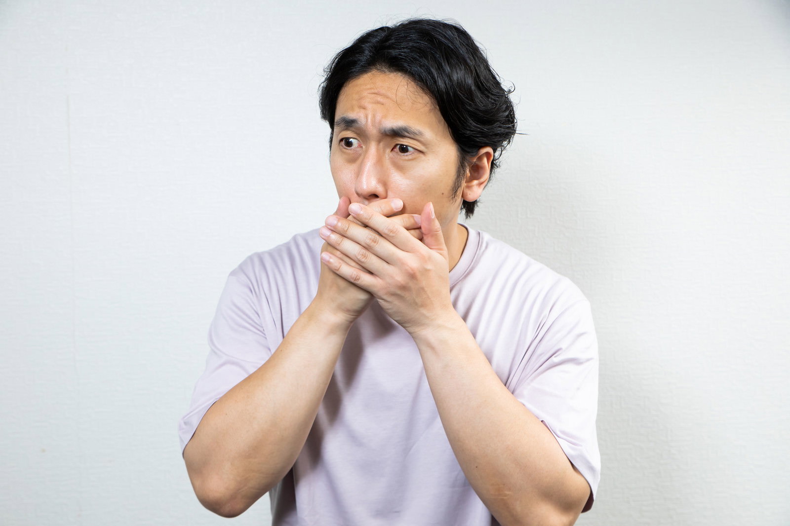 白いTシャツを着た男性が両手で口を覆い驚愕している様子［モデル：大川竜弥］