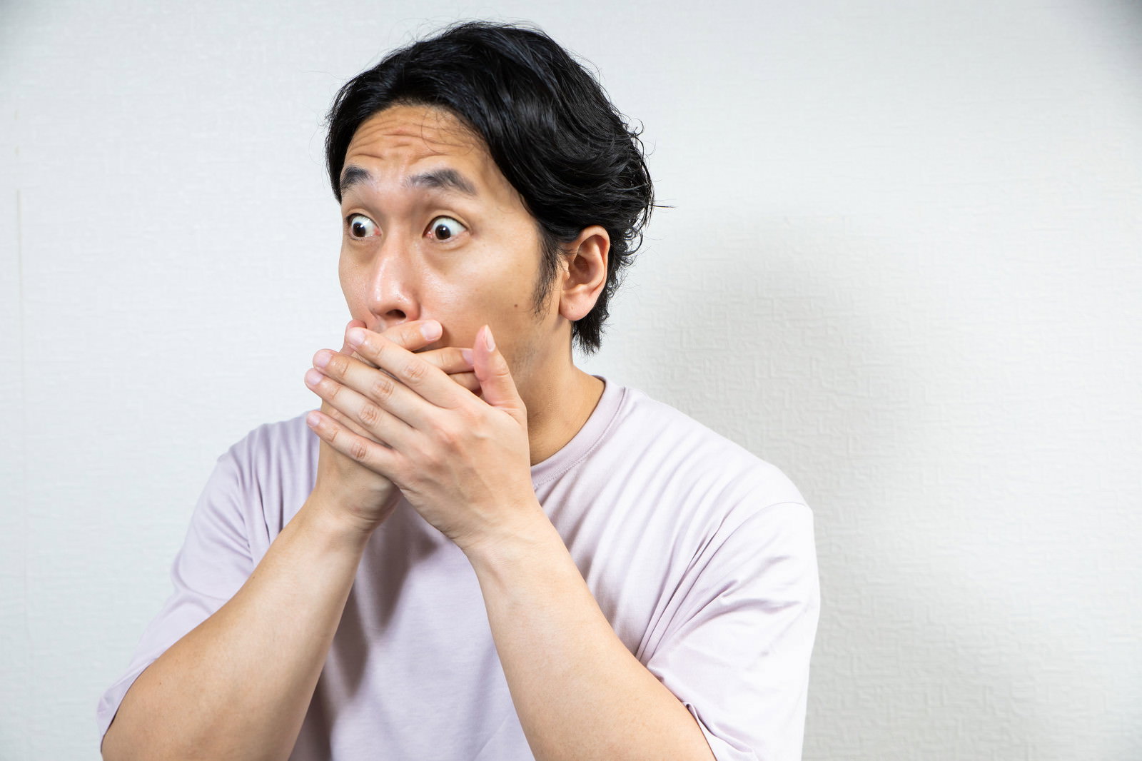両手で口を覆いながら驚いた表情の男性［モデル：大川竜弥］
