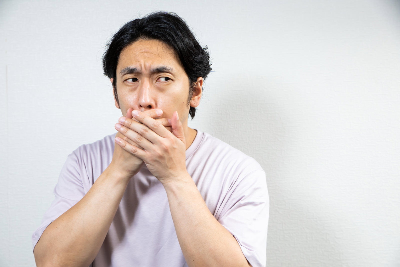 口を両手で覆き、眉をひそめて上を見つめる男性［モデル：大川竜弥］