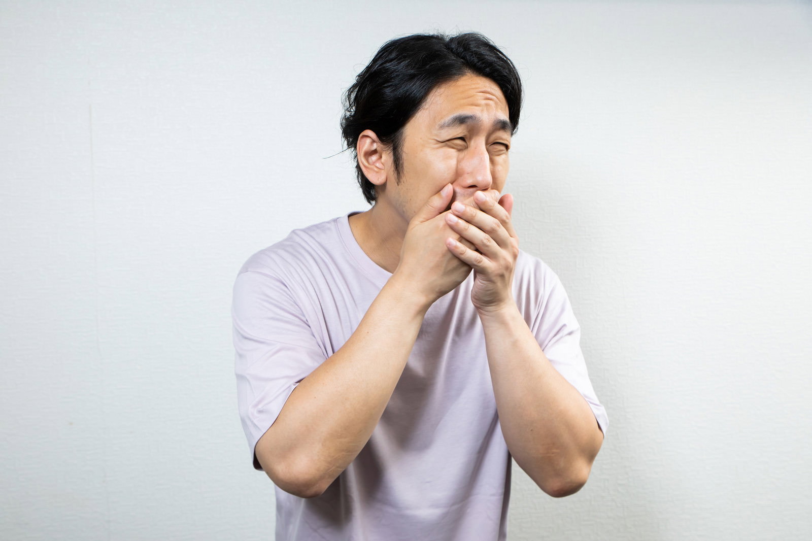 両手で口元を覆いながら眉をひそめた表情の男性［モデル：大川竜弥］
