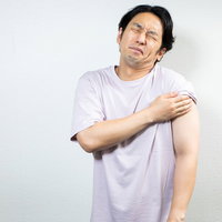 ワクチン接種後に左腕を抑えて困った表情を見せる男性の写真