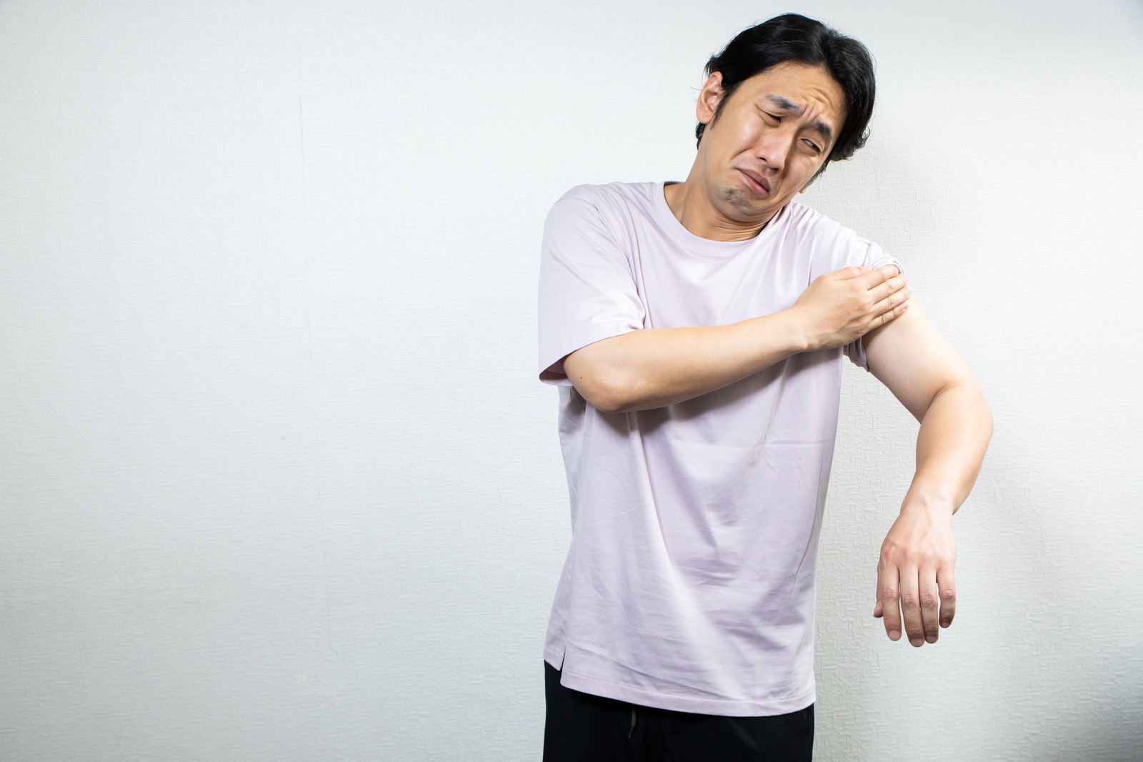 白いTシャツを着た男性がワクチン接種の痛みで顔をしかめている［モデル：大川竜弥］