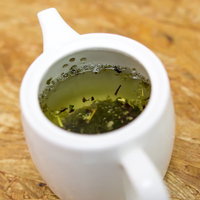 白い急須に入った緑茶と茶葉の写真