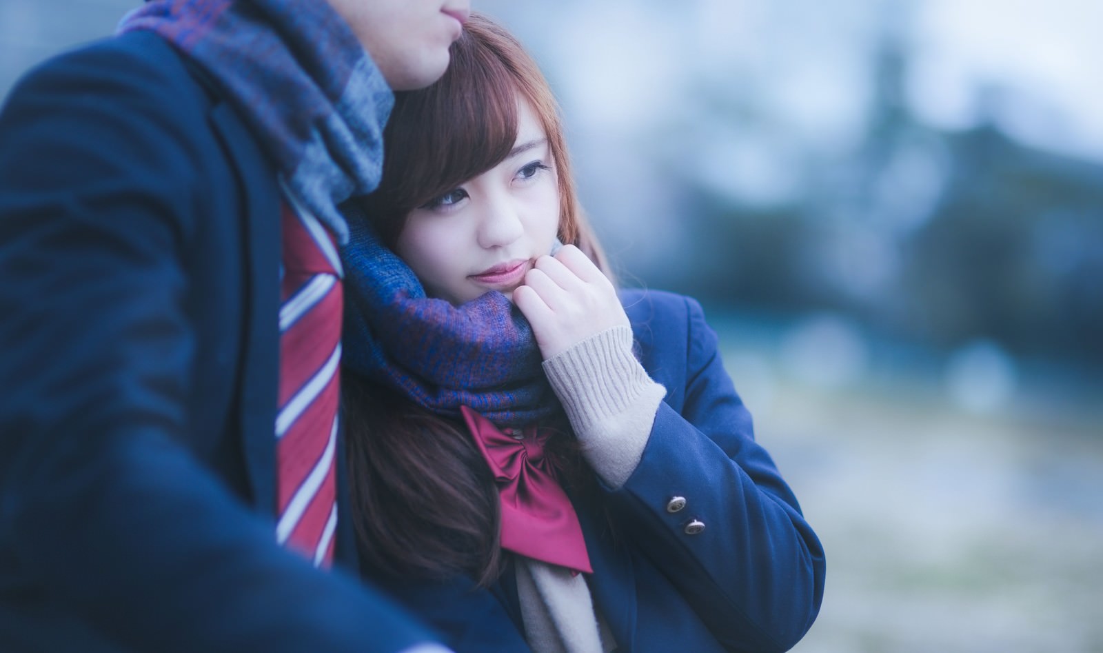 青いマフラーを口元に当てる茶髪女性と隣の青い制服の人物［モデル：河村友歌］
