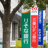 銀行や金融系のニュースが話題になると使われるメガバンクの看板と街路樹の写真