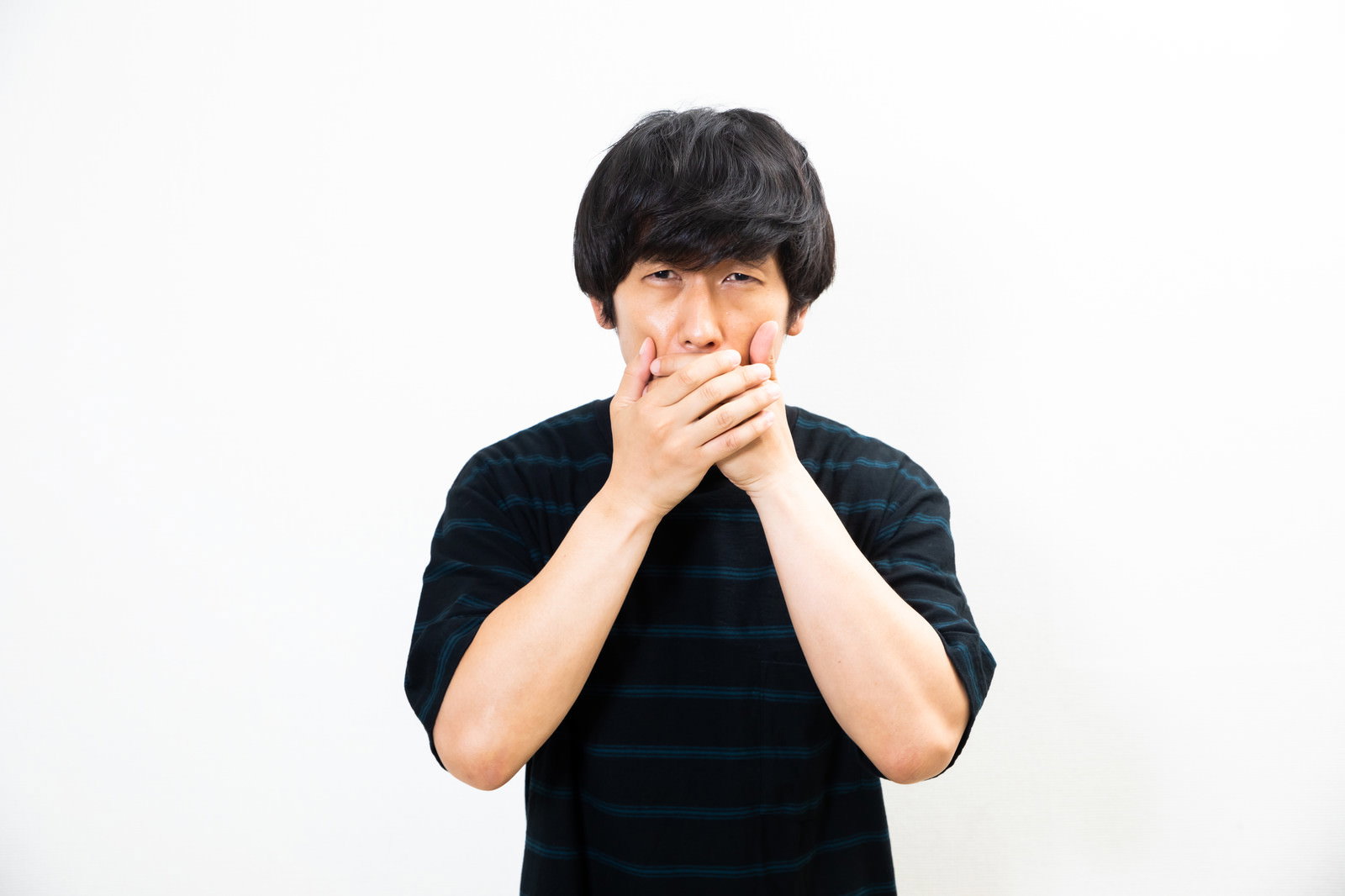 黒いTシャツを着た男性が両手で口を覆って驚いている様子［モデル：大川竜弥］