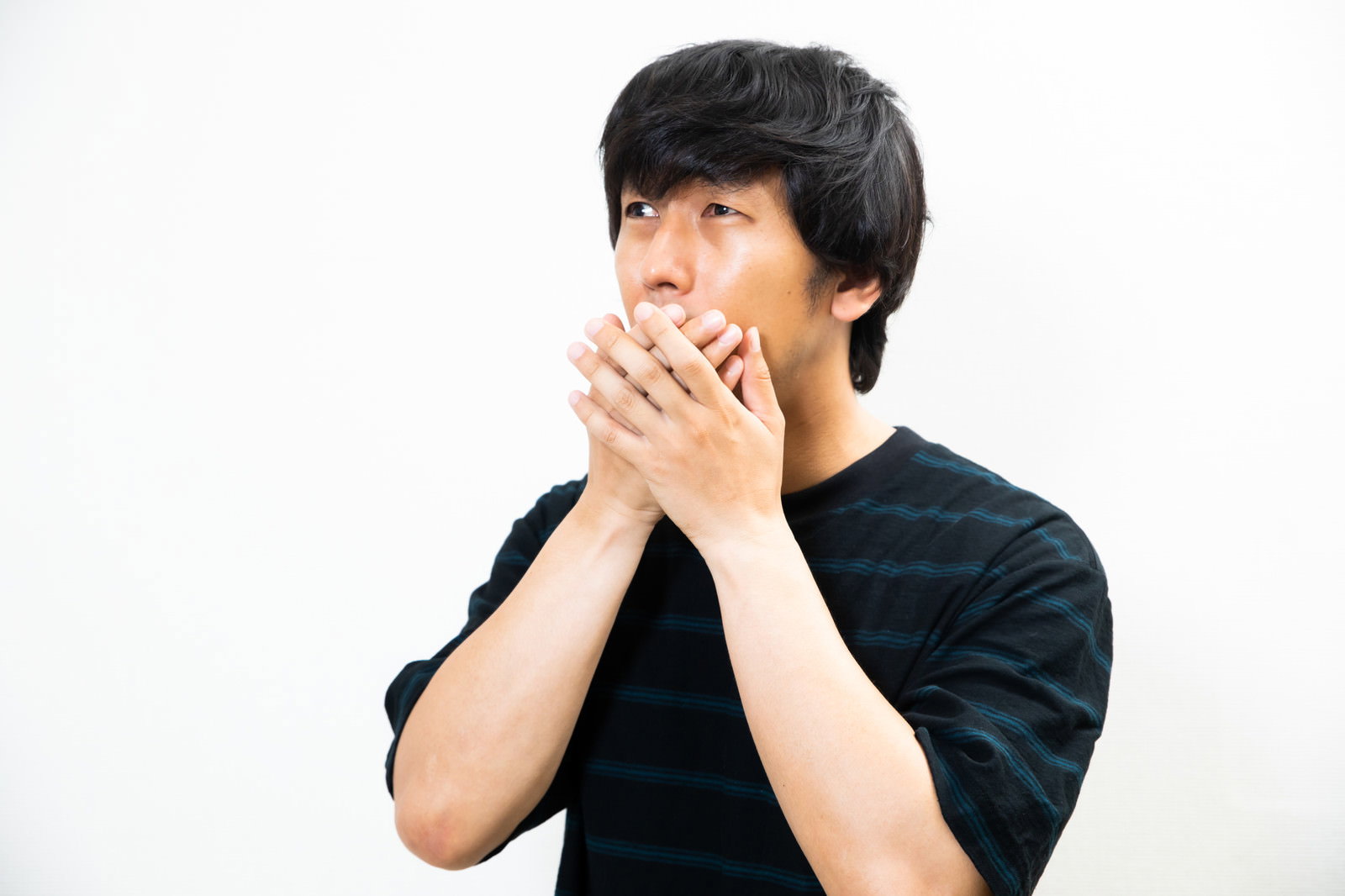 両手で口元を覆い驚いた表情を見せる黒いTシャツの男性［モデル：大川竜弥］