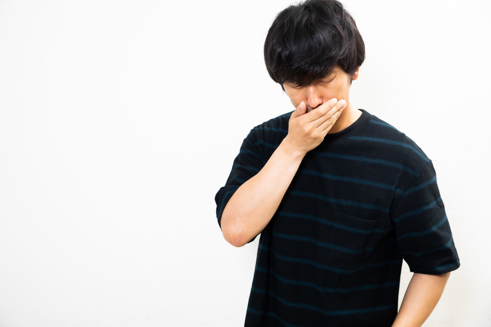 黒いTシャツを着た男性が手で口元を覆っている様子［モデル：大川竜弥］