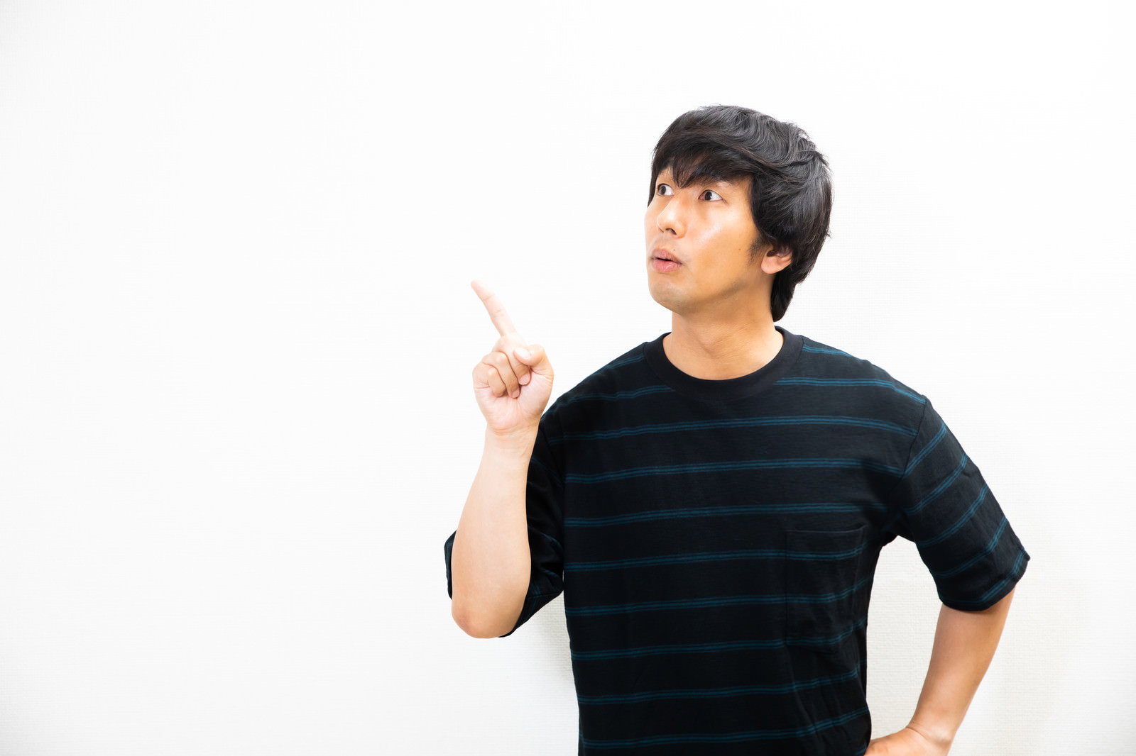 驚いた表情で右手の人差し指で何かを指している黒いシャツの男性［モデル：大川竜弥］