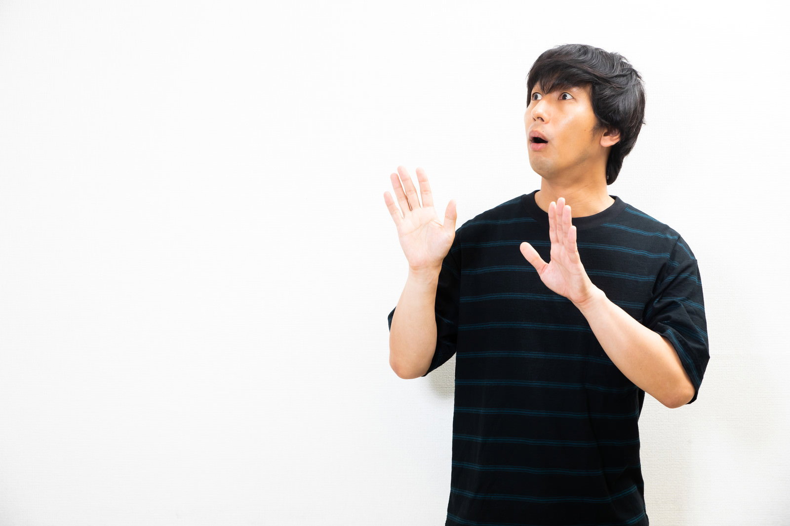 黒いTシャツを着た男性が驚いた表情で両手を上げて後ずさりしている様子［モデル：大川竜弥］