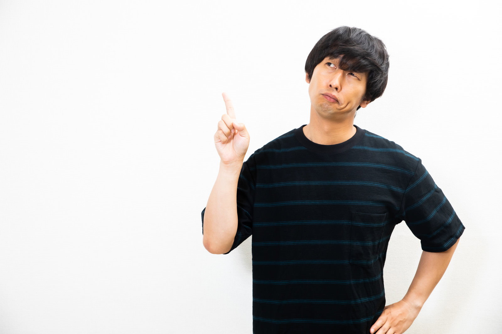 上を指さして不満そうな表情を浮かべる黒いTシャツの男性［モデル：大川竜弥］