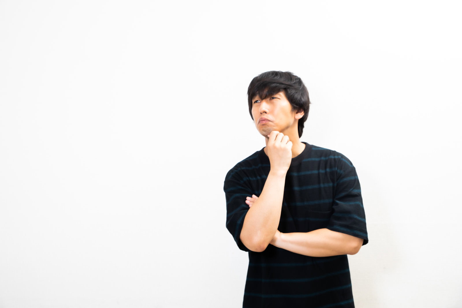 黒い服を着た男性が顎に手を当てて考え込んでいる［モデル：大川竜弥］