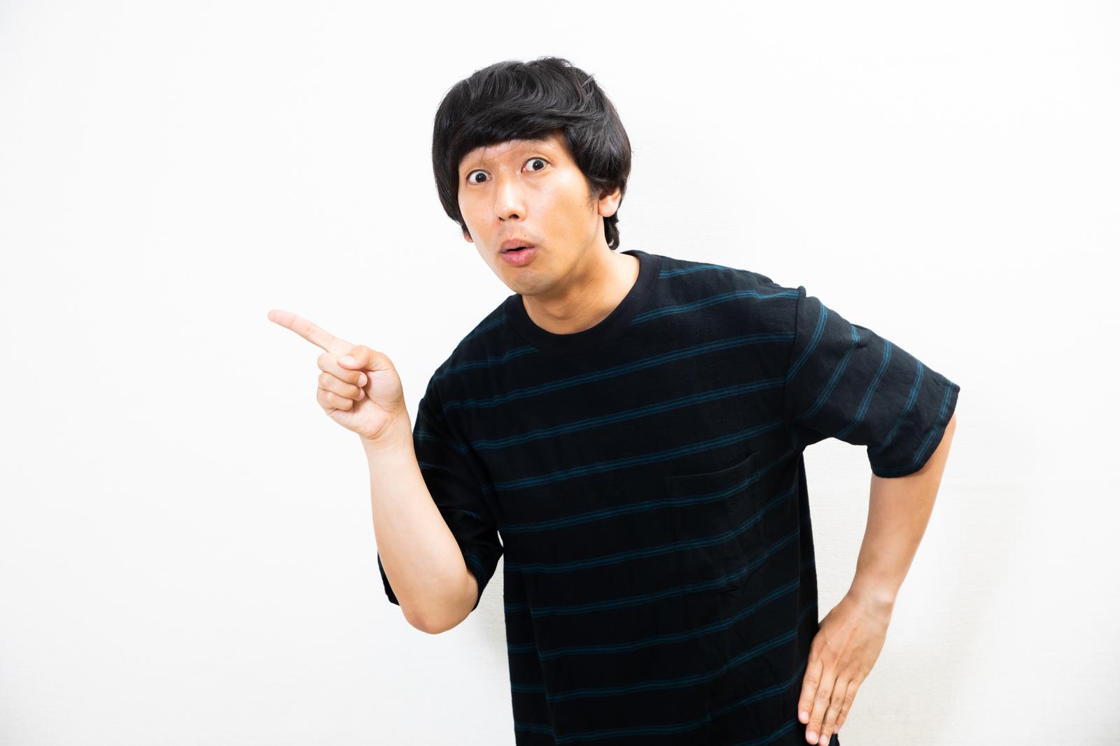 黒と青のボーダーシャツを着た男性が左を指差して驚いた表情をしている［モデル：大川竜弥］