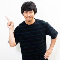 人差し指を立てて注目を向ける黒いストライプシャツの男性の写真