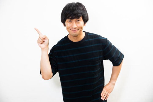 人差し指を立てて注目を向ける黒いストライプシャツの男性