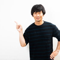 笑みを浮かべながら右手で指差し説明する男性の写真