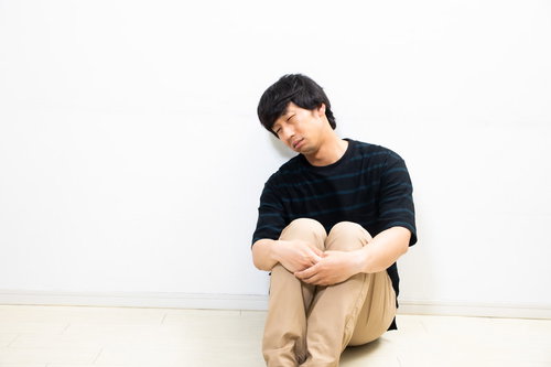 膝を抱えて不貞腐れる男性の疲労感と心身の疲弊