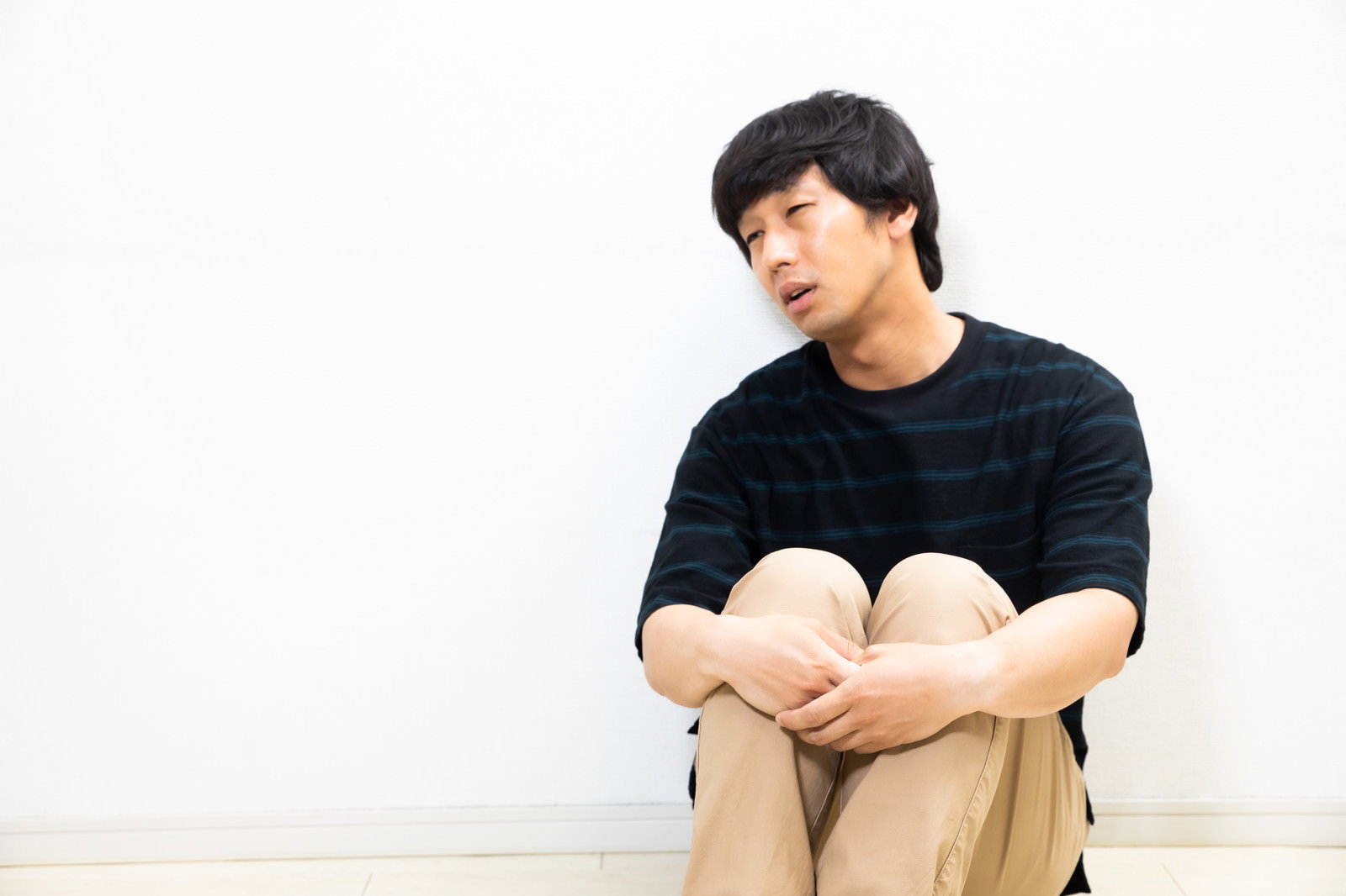 黒のストライプシャツを着た男性が膝を抱えて座り込んでいる［モデル：大川竜弥］