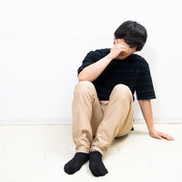 顔を覆い落ち込む男性の体育座り姿勢の写真