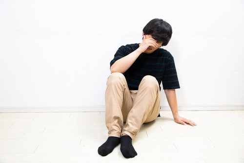 顔を覆い落ち込む男性の体育座り姿勢