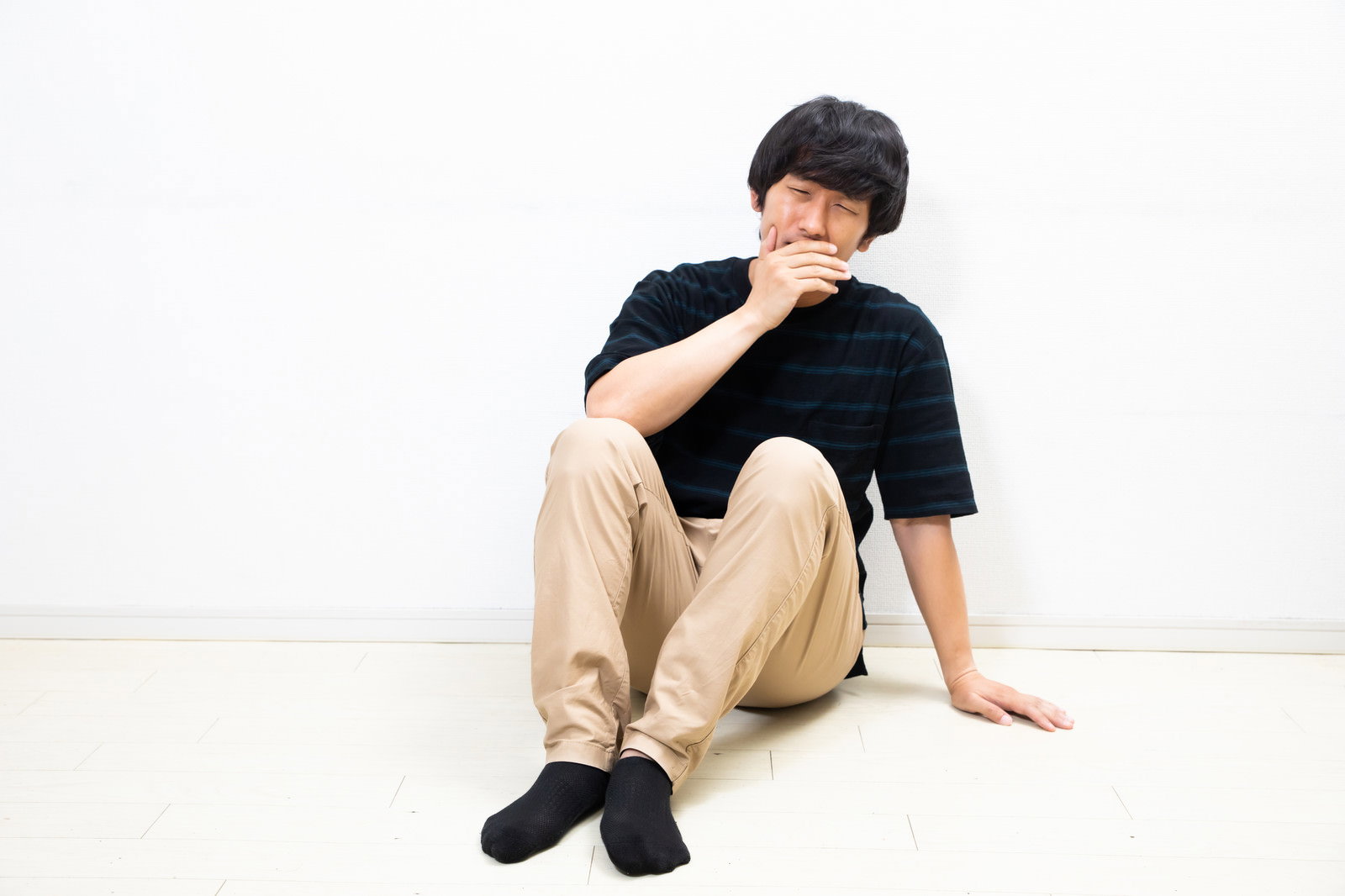 黒いTシャツを着た男性が床に座り膝を抱えている様子［モデル：大川竜弥］