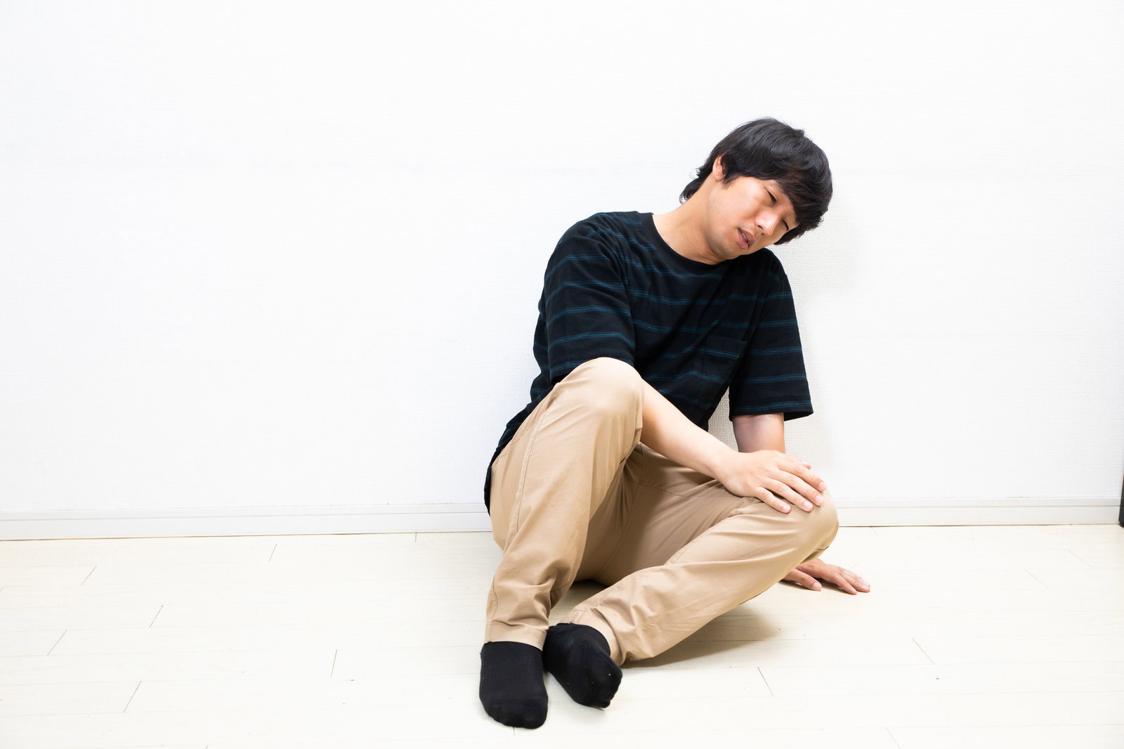 壁際に座り込んでうなだれている黒い服の男性［モデル：大川竜弥］