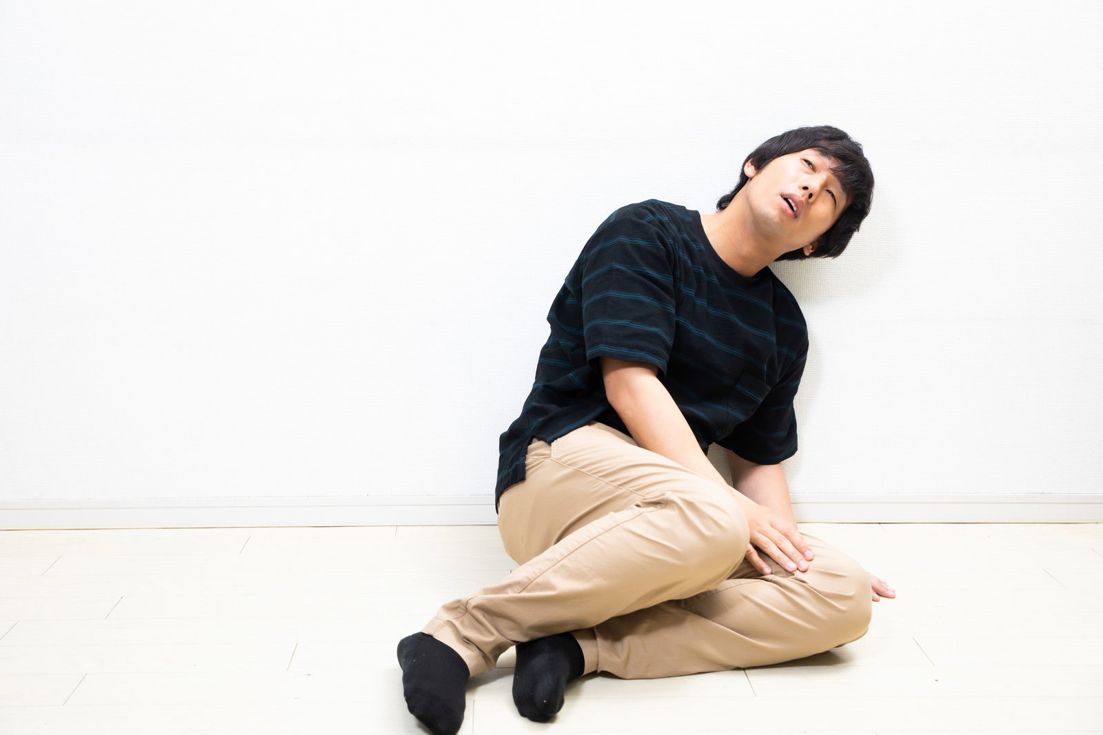 床に座り込み天を仰ぐ黒い服を着た男性［モデル：大川竜弥］