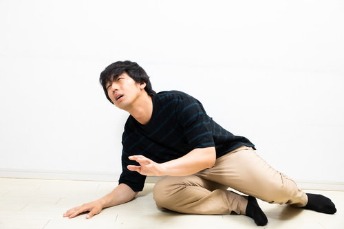 ぎっくり腰で床に座り込む落ち込む男性