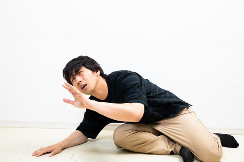 床に蹲り片手を上げて助けを乞う男性の苦しい表情