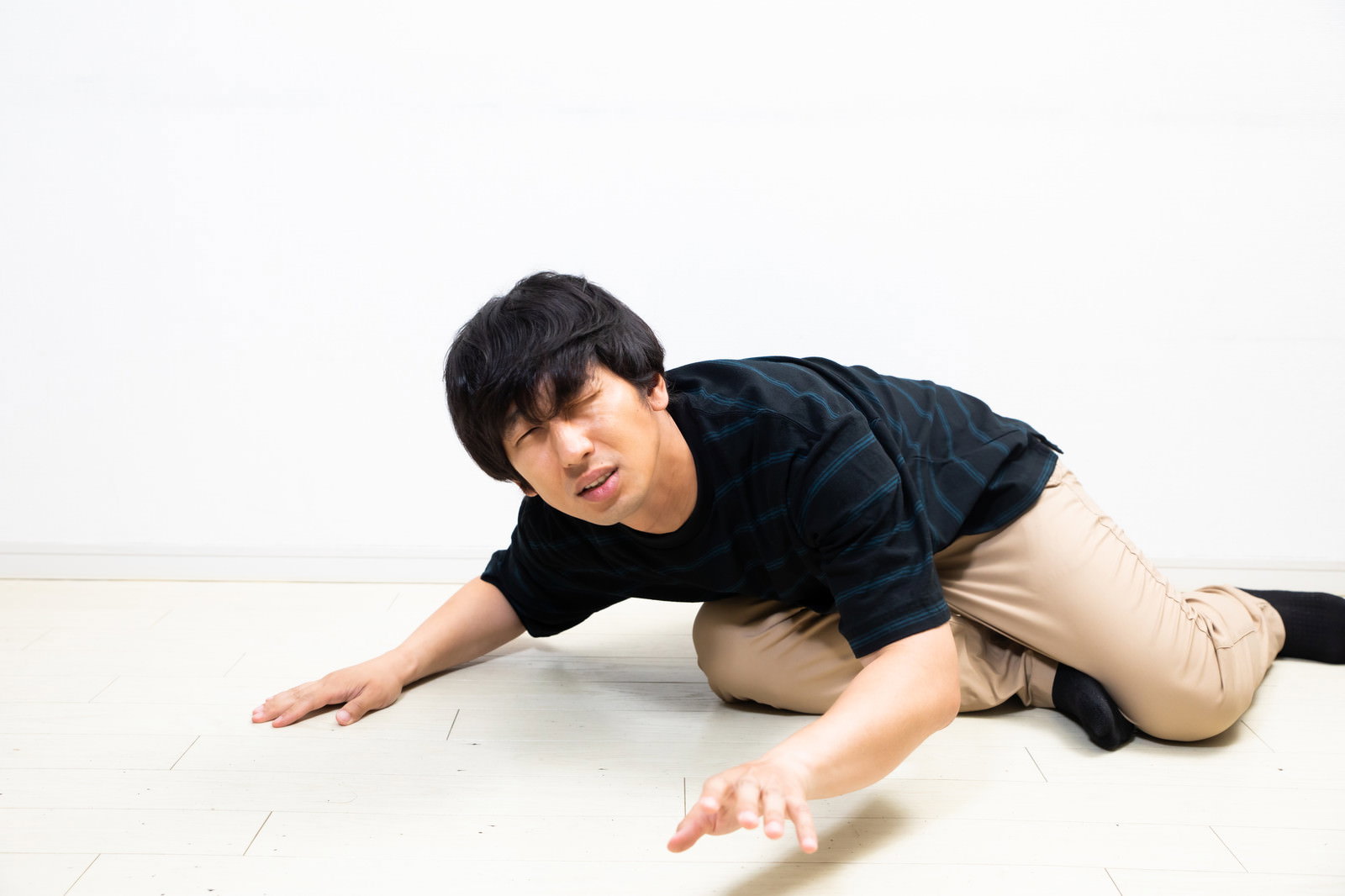 白い床に座り込み、両手を床について深くうつむいている男性［モデル：大川竜弥］