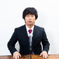 演壇で謝罪する男性の記者会見での謝罪シーンの写真